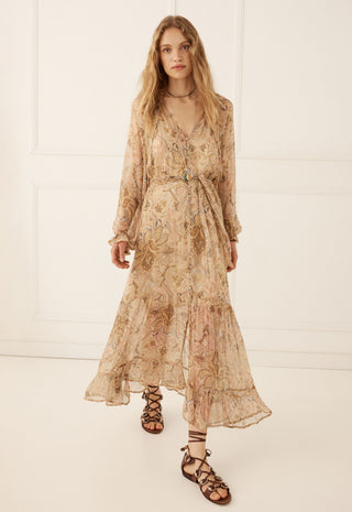 a-woman-modeling-a-long-sleeved-v-neck-maxi-dress-with-a-beige-and-brown-floral-pattern-paired-with-brown-lace-up-sandals-set-against-a-white-paneled-wall