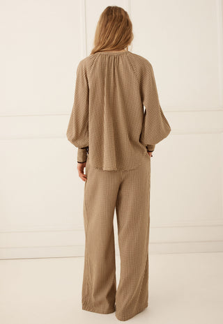 a-woman-viewed-from-the-back-wearing-a-matching-beige-and-brown-checkered-two-piece-set-consisting-of-a-long-sleeve-blouse-with-balloon-sleeves-and-wide-leg-trousers-set-against-a-clean-white-paneled-studio-background