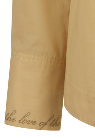 Close-up of a beige or tan fabric garment sleeve with cursive text reading 'the love of the' printed near the cuff on a white background.