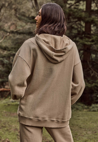 a-woman-wearing-an-oversized-taupe-brown-hooded-sweatshirt-and-matching-sweatpants-photographed-from-behind-in-an-outdoor-forest-setting