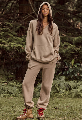 a-woman-stands-outdoors-in-a-wooded-setting-wearing-a-matching-beige-hooded-sweatshirt-and-jogger-pants-set-with-red-lace-up-ankle-boots