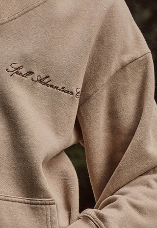 close-up-of-a-beige-crewneck-sweatshirt-with-dark-brown-embroidered-script-on-the-chest-reading-spell-adventures